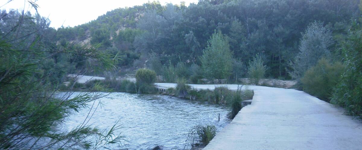 A concrete bridge over a river with surrounding greenery and hills.