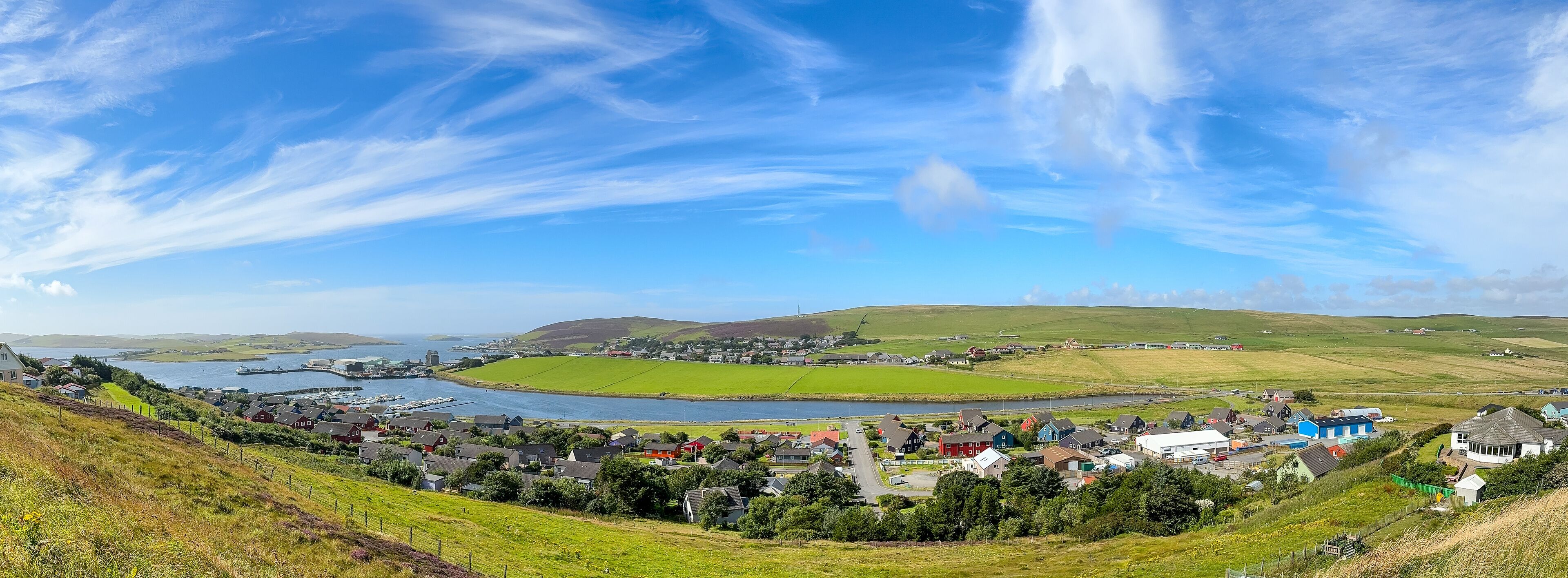 A coastal town with a harbor, green fields, and rolling hills.