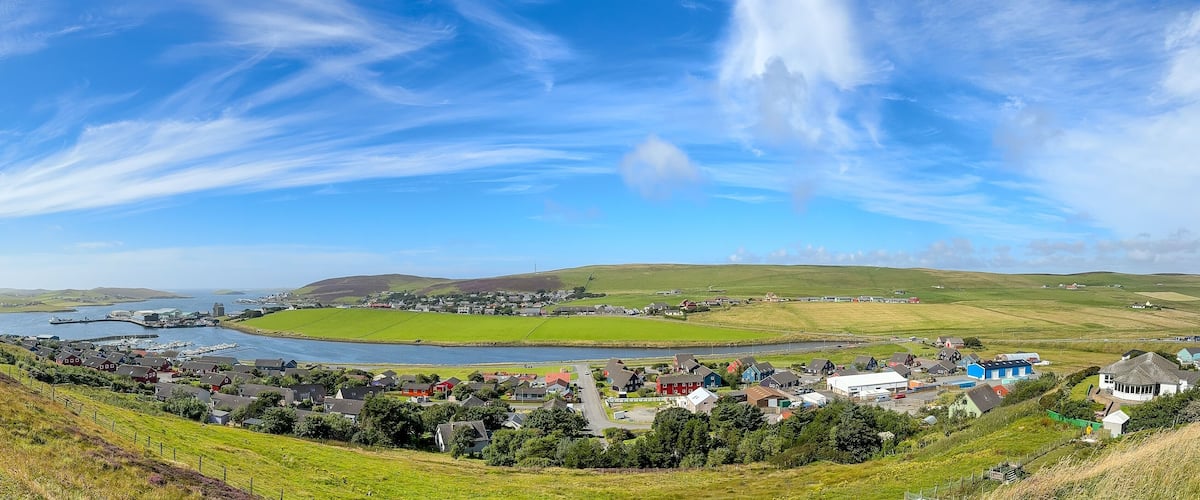 A coastal town with a harbor, green fields, and rolling hills.