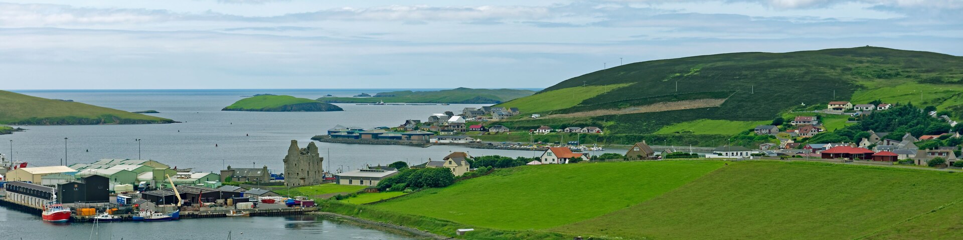 Un pueblo costero con un puerto, barcos y colinas verdes.