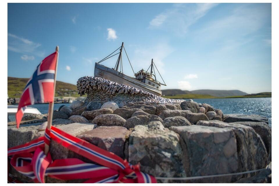 Un model de vaixell a la riba rocosa amb una bandera al primer pla.