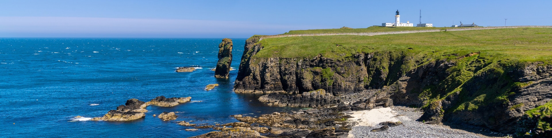 Un paisaje costero con un faro, acantilados rocosos y aguas azules cristalinas.