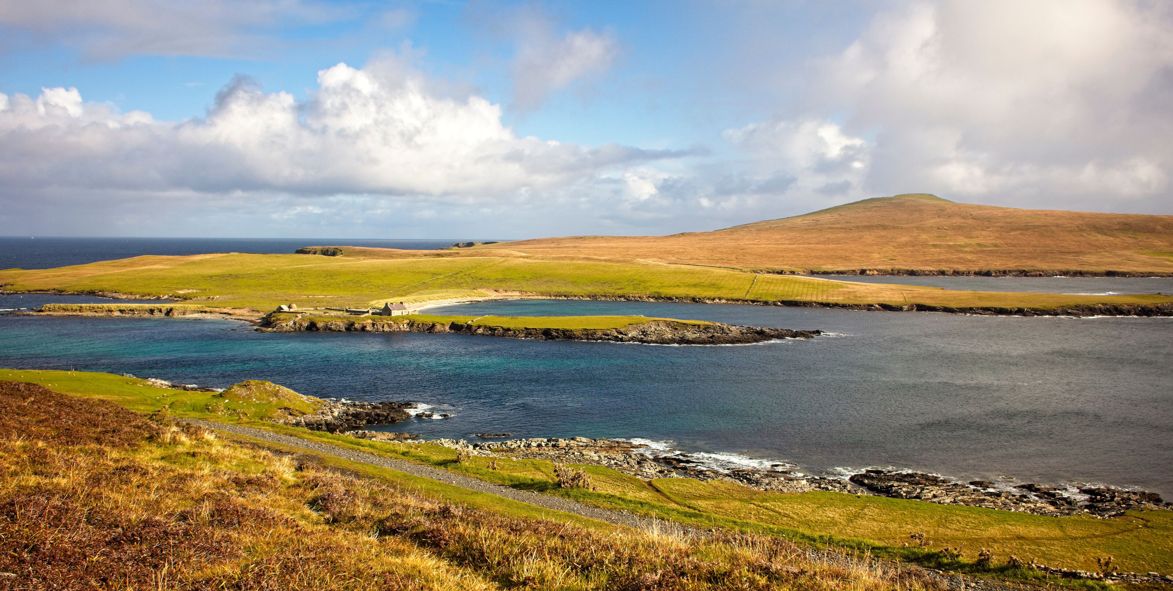 A coastal landscape with a grassy hill, a small settlement, and a body of water.