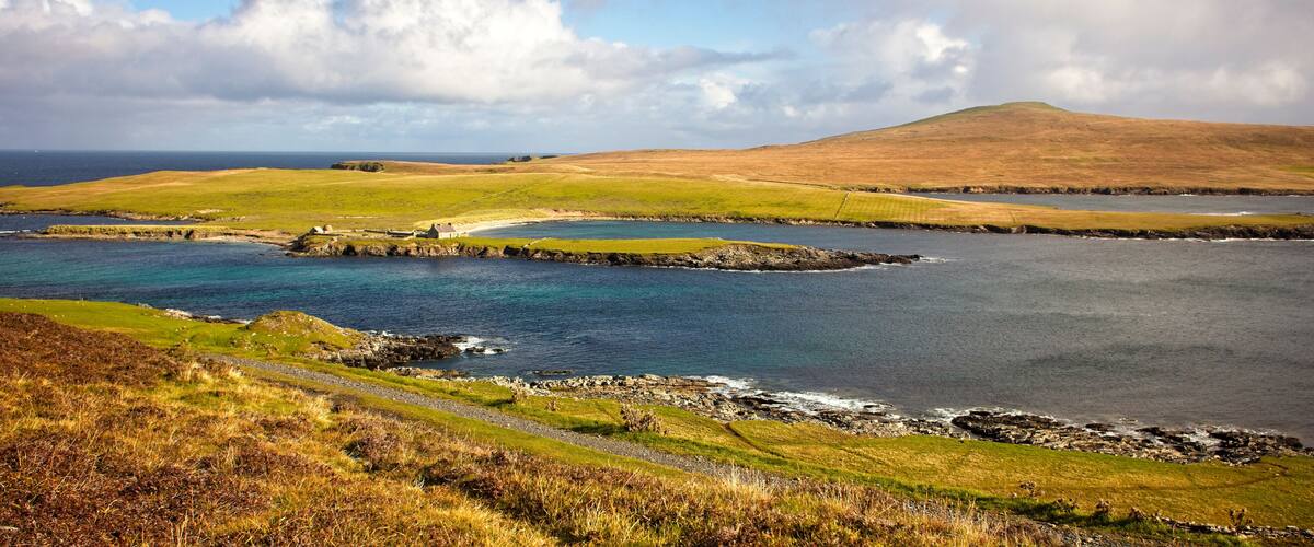 A coastal landscape with a grassy hill, a small settlement, and a body of water.