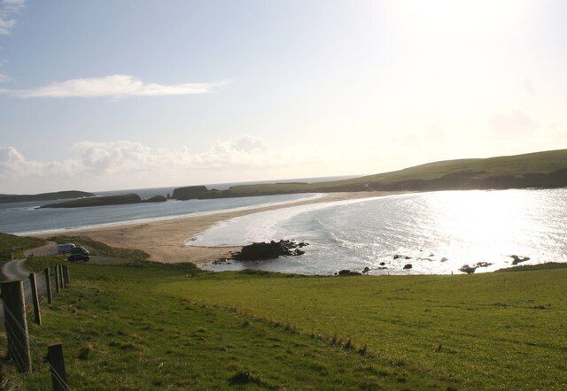 A coastal landscape with a grassy foreground, a sandy beach, and a calm sea.