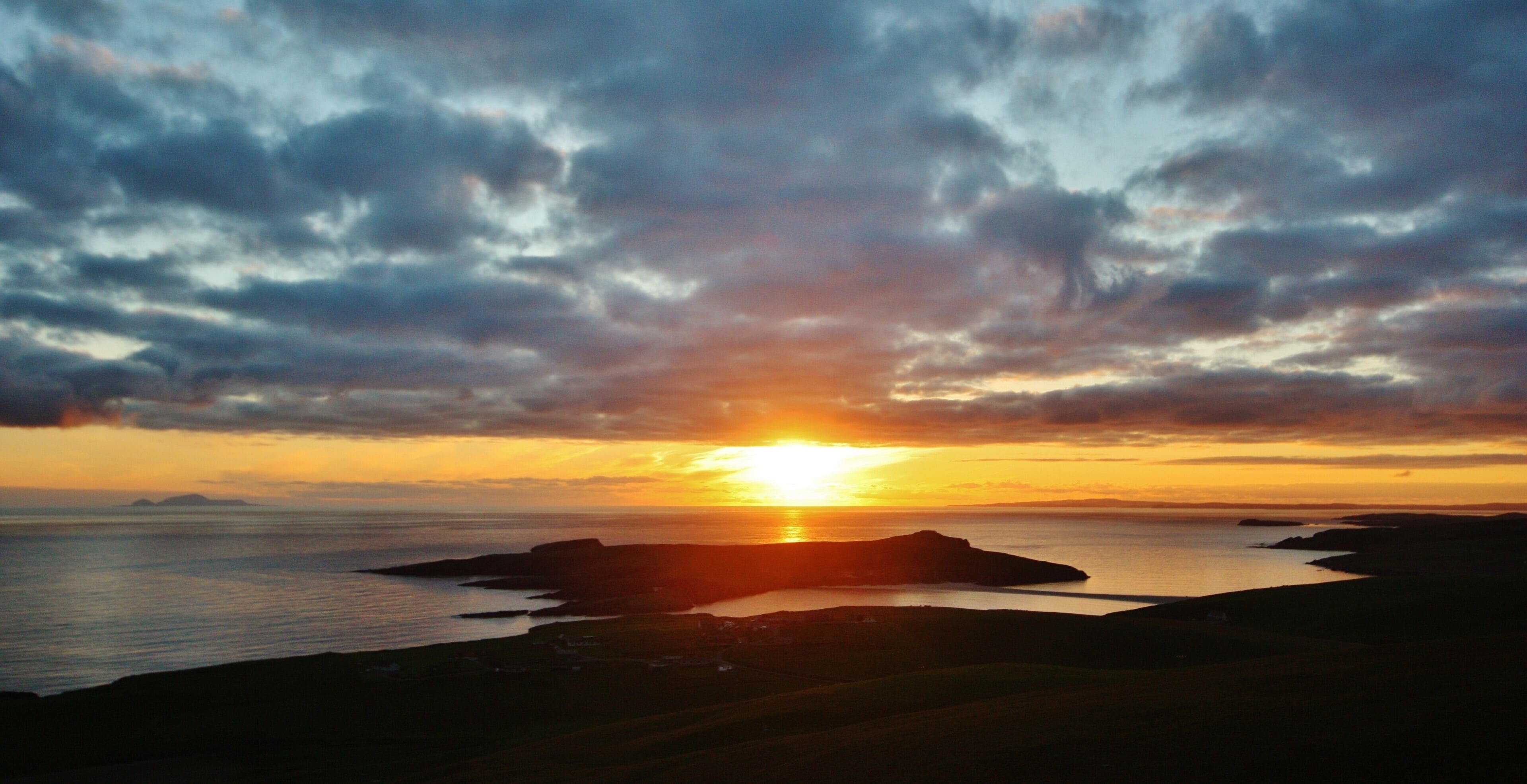 A sunset over a coastal landscape with cliffs and a body of water.