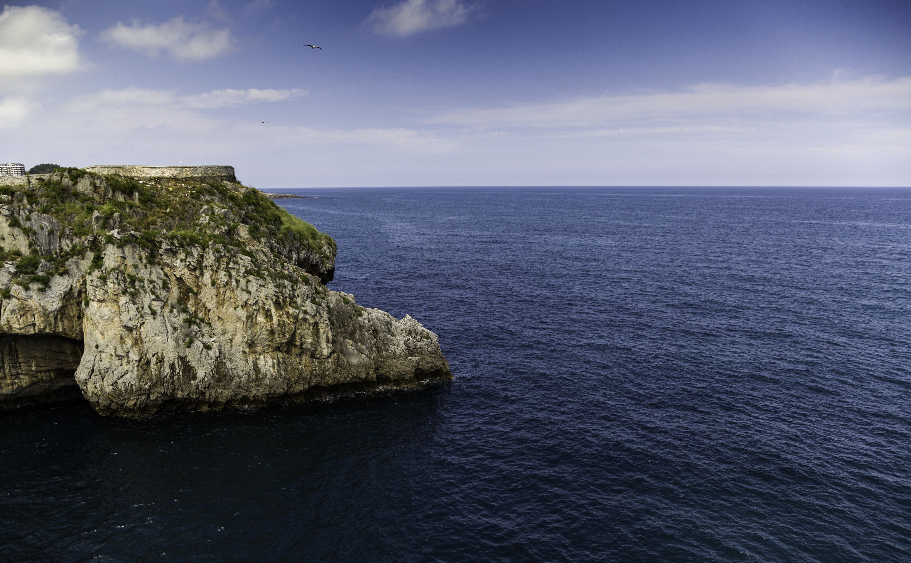 A rocky coastline with a fortification on a cliff overlooking the sea.