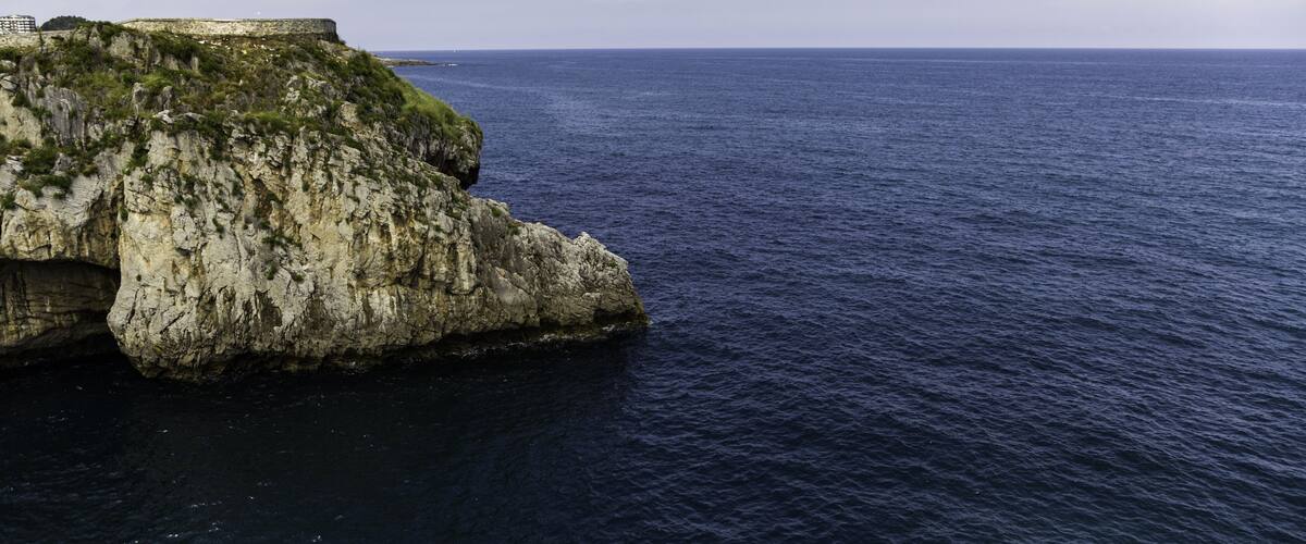 A rocky coastline with a fortification on a cliff overlooking the sea.