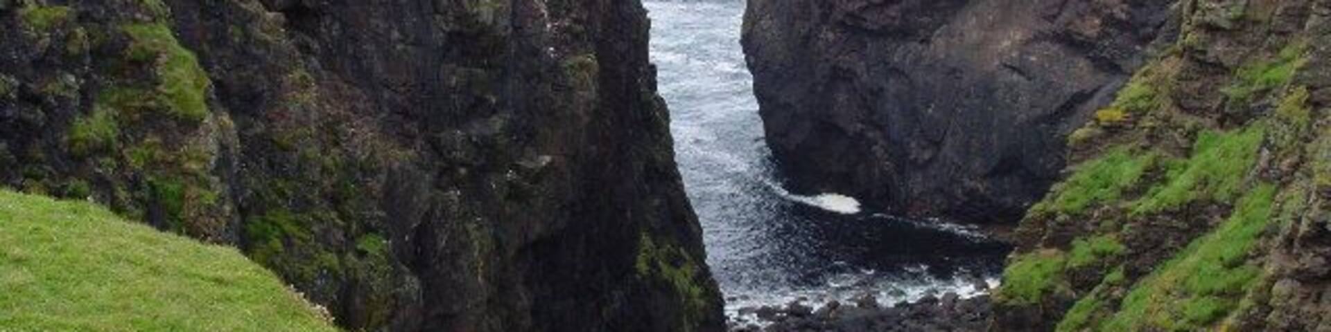 A coastal cliff with a narrow passage leading to the sea.
