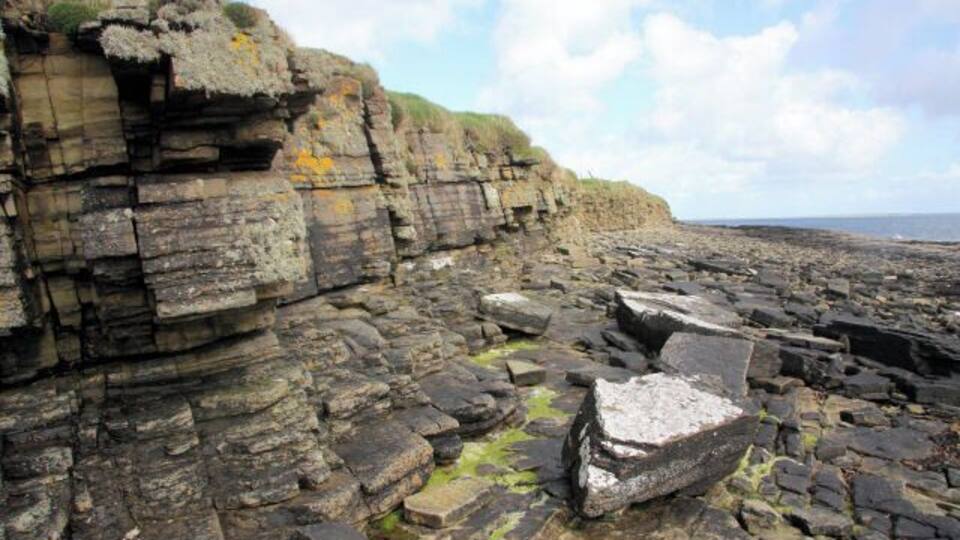A rocky coastal landscape with layered cliffs and scattered boulders.