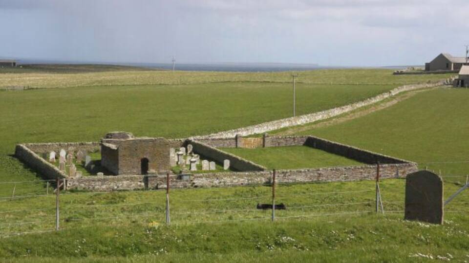 A rural landscape with a stone structure, possibly ruins, and a fenced graveyard.