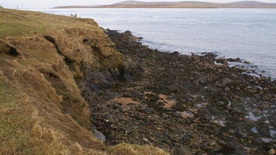 A rocky shoreline with grass-covered cliffs and calm water.