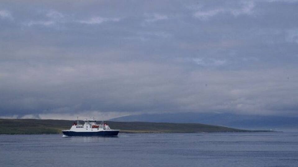 A boat on calm water with a cloudy sky and distant land.