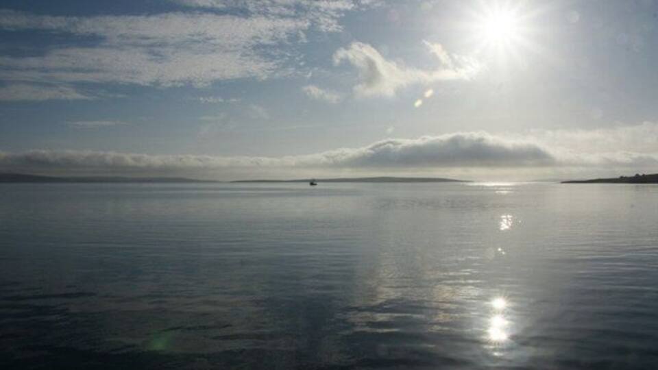 A calm body of water with a clear sky and the sun shining.