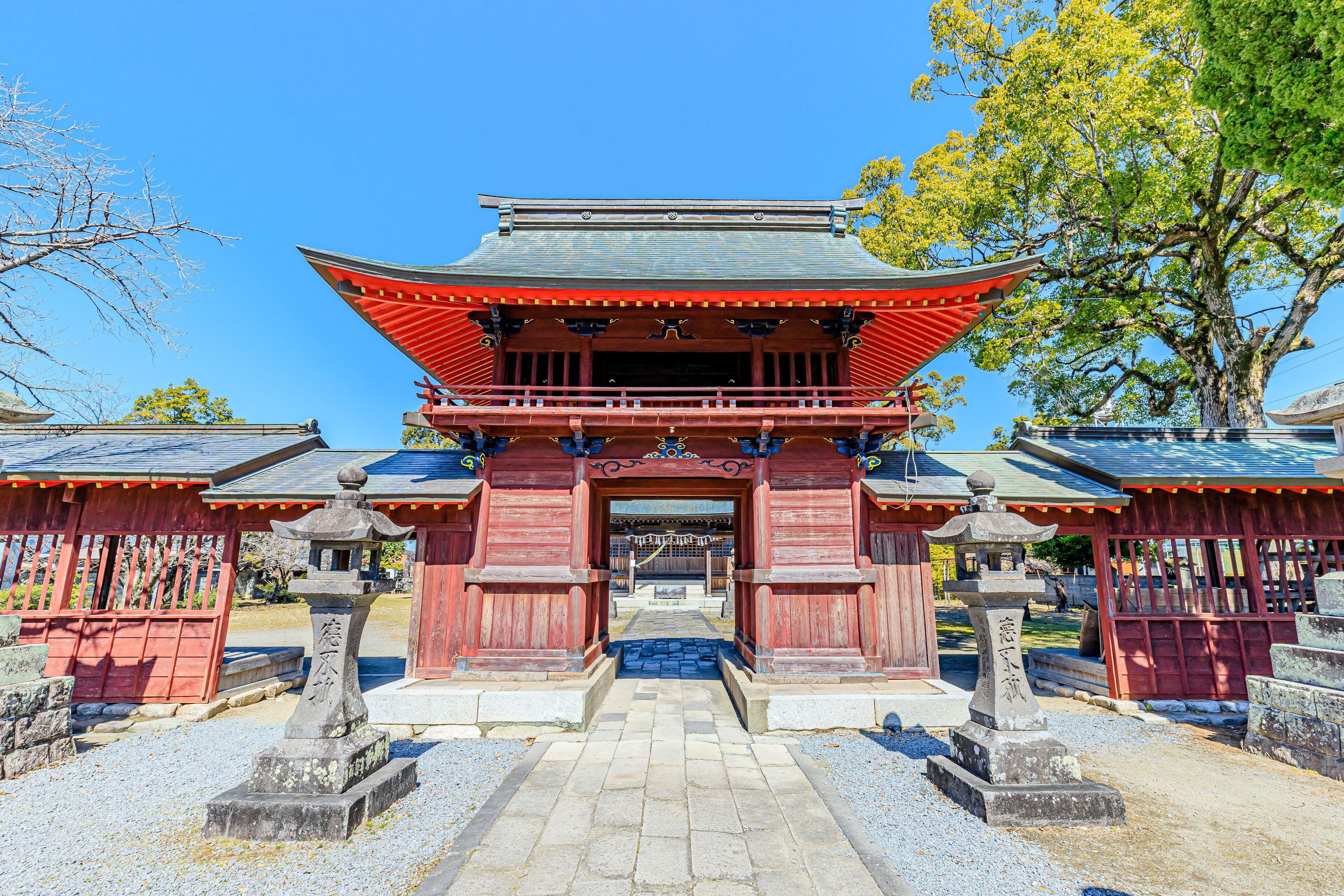 A traditional Japanese temple with a red gate, stone lanterns, and a clear blue sky.