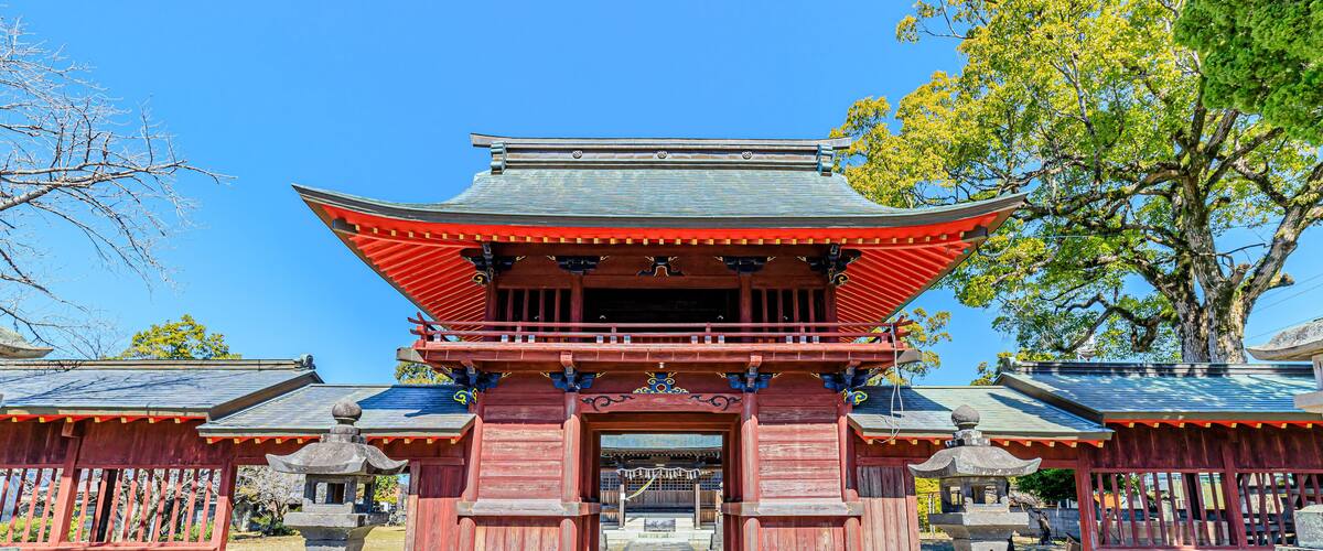 A traditional Japanese temple with a red gate, stone lanterns, and a clear blue sky.