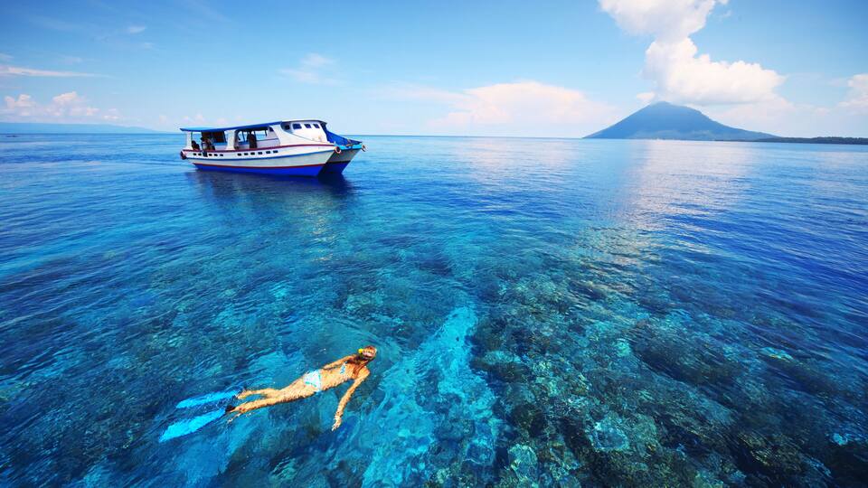 A clear blue sea with a boat and a diver.