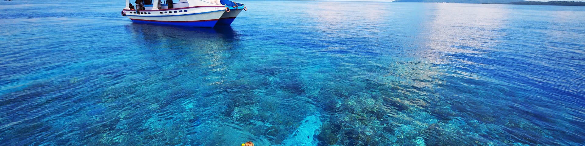 Young woman snorkeling in transparent shallow sea near boat