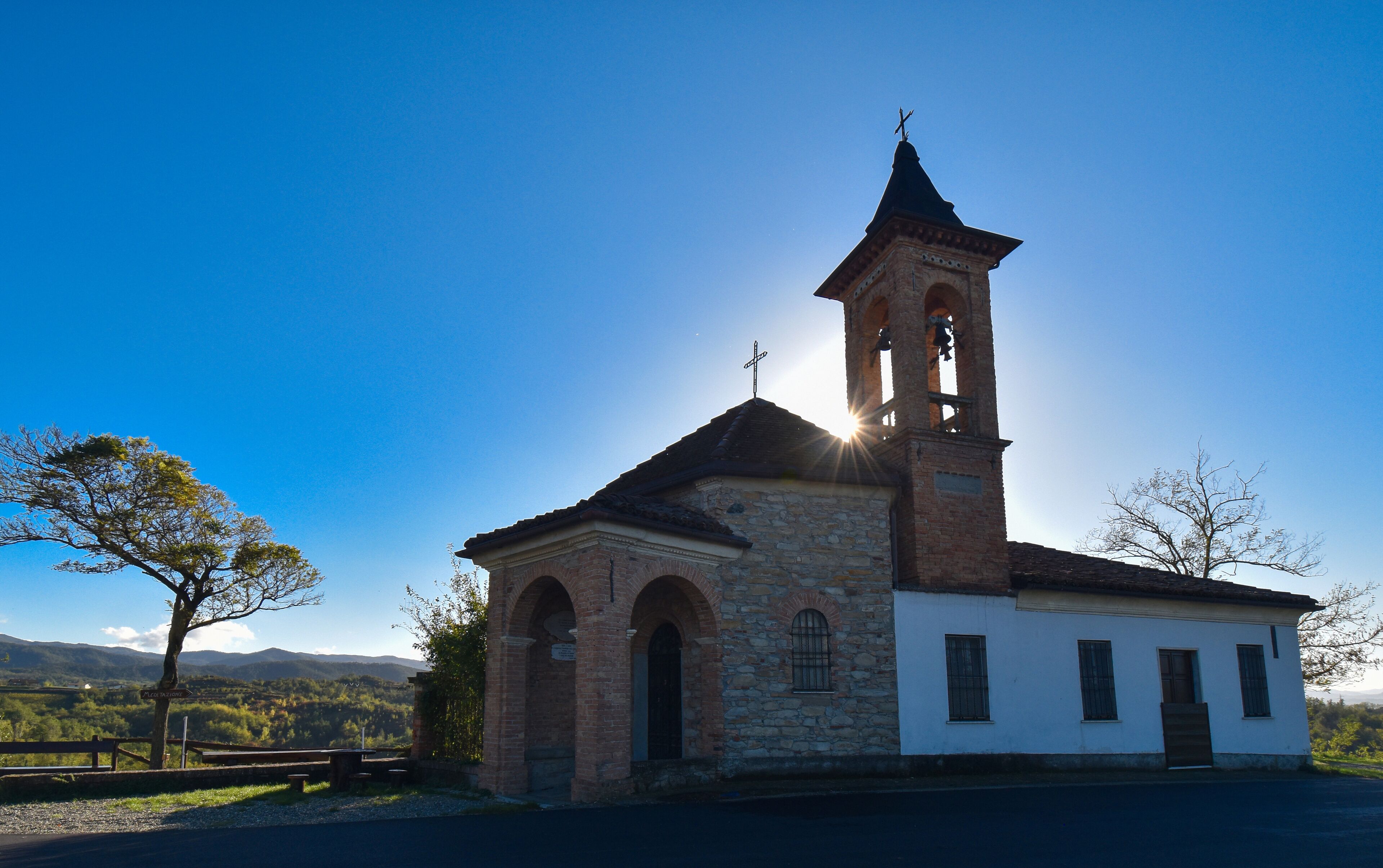 A church with a bell tower and a cross on top, surrounded by trees and mountains in the background.