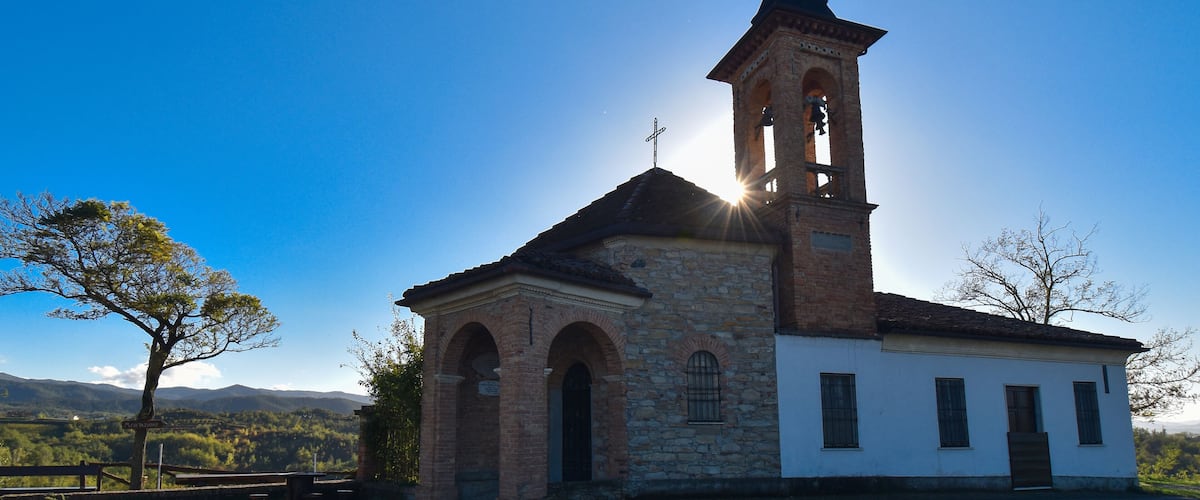 A church with a bell tower and a cross on top, surrounded by trees and mountains in the background.