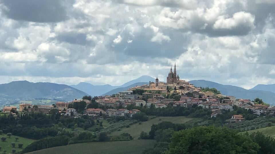 A historic town with a prominent church on a hill, surrounded by greenery and mountains.
