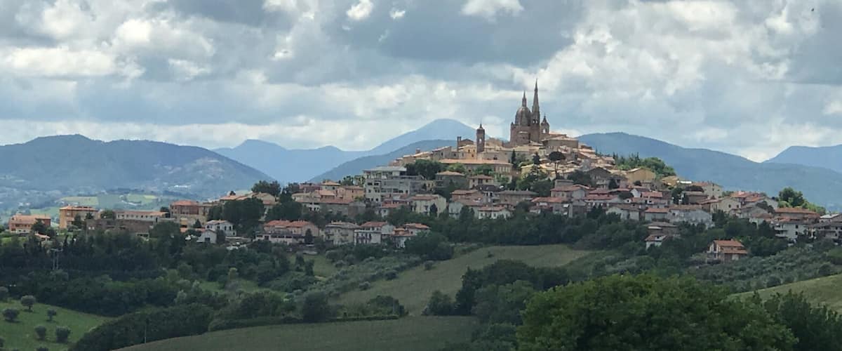 A historic town with a prominent church on a hill, surrounded by greenery and mountains.