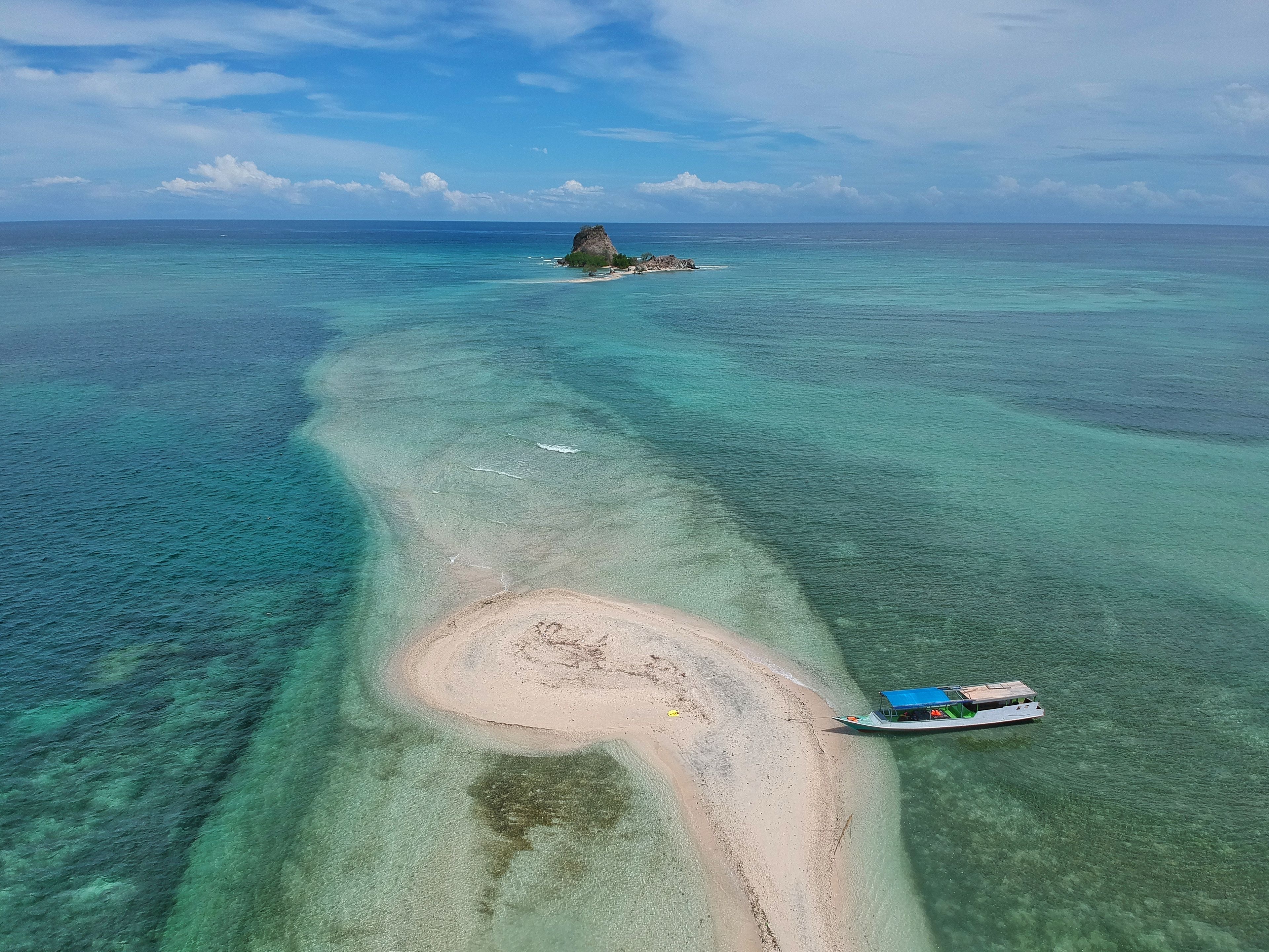 A boat on a turquoise beach with clear water and a small island in the distance.