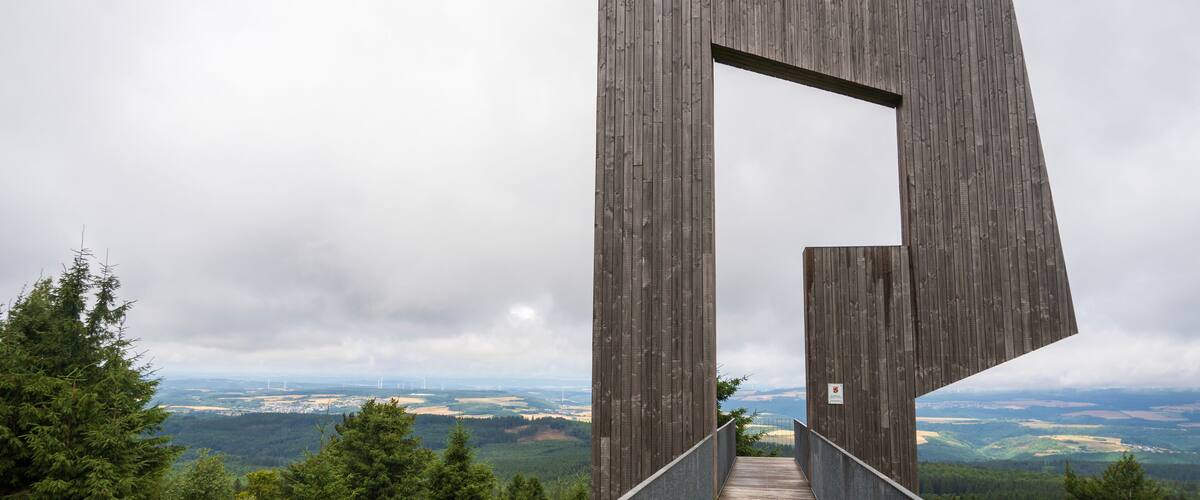 A wooden bridge with a unique design, leading to a scenic overlook with a view of distant landscapes.
