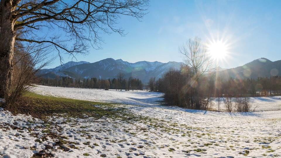 A snow-covered landscape with a road, trees, and mountains in the background.