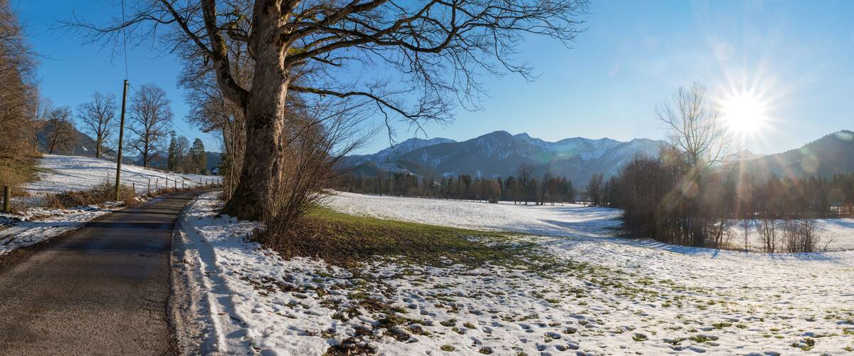 A snow-covered landscape with a road, trees, and mountains in the background.