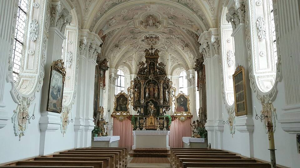 An ornate church interior with high ceilings, detailed frescoes, and a central altar.