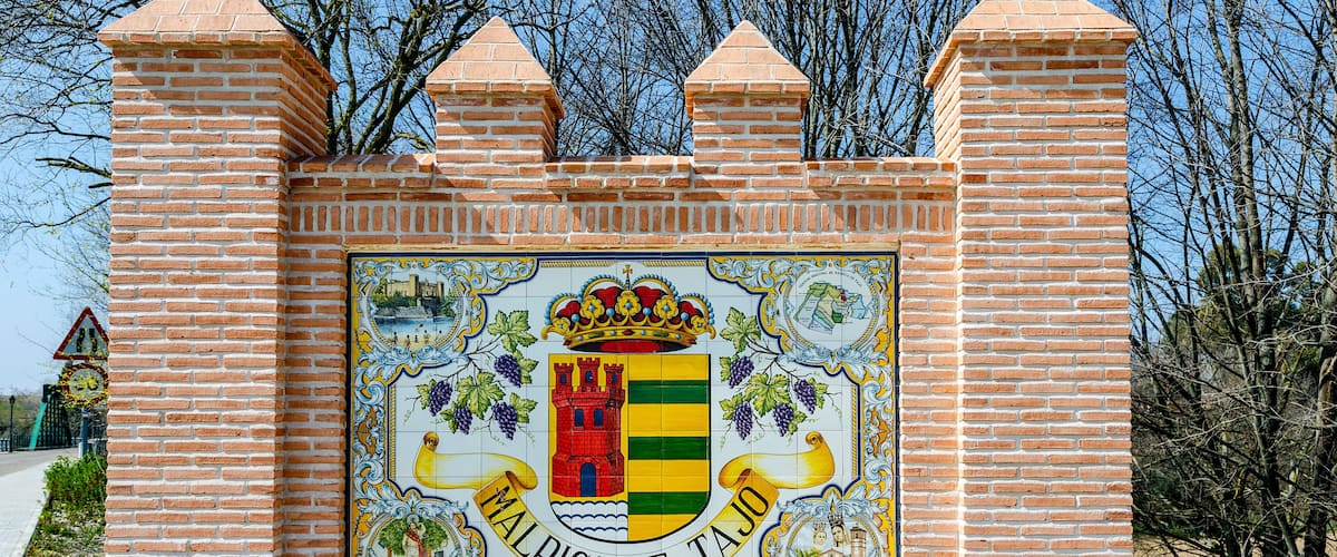 A brick wall with a colorful coat of arms and the text "MALPICA DE TAJO".