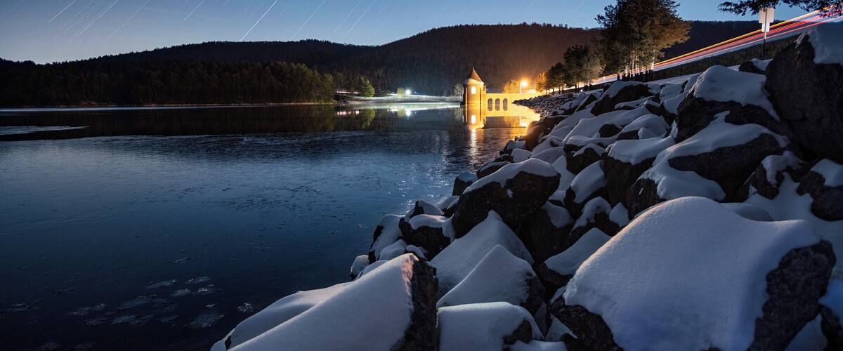 A snow-covered landscape with a lit tower by a lake at night.