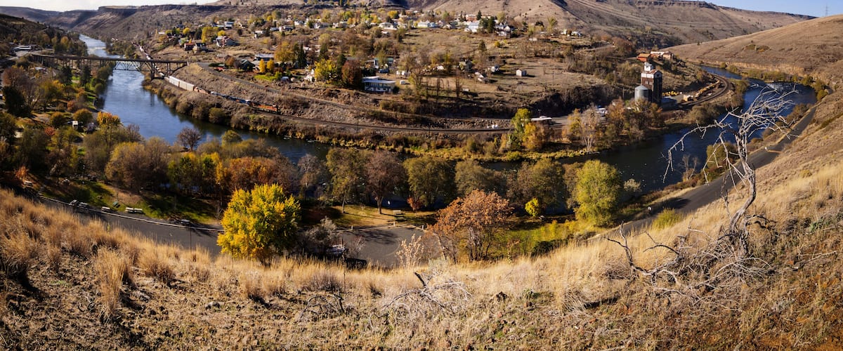 A town by a river with a bridge, surrounded by hills and sparse vegetation.