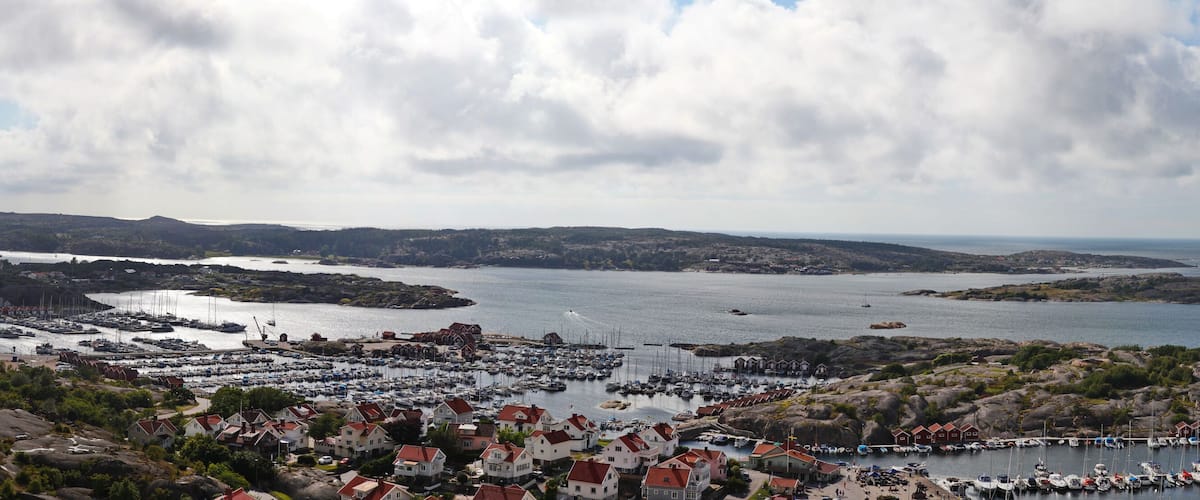 A coastal town with a marina, houses, and rocky islands in the background.