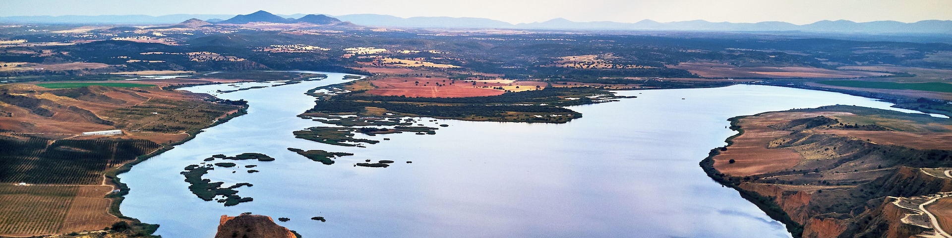 Un río serpenteando por un valle, con colinas circundantes y montañas distantes.