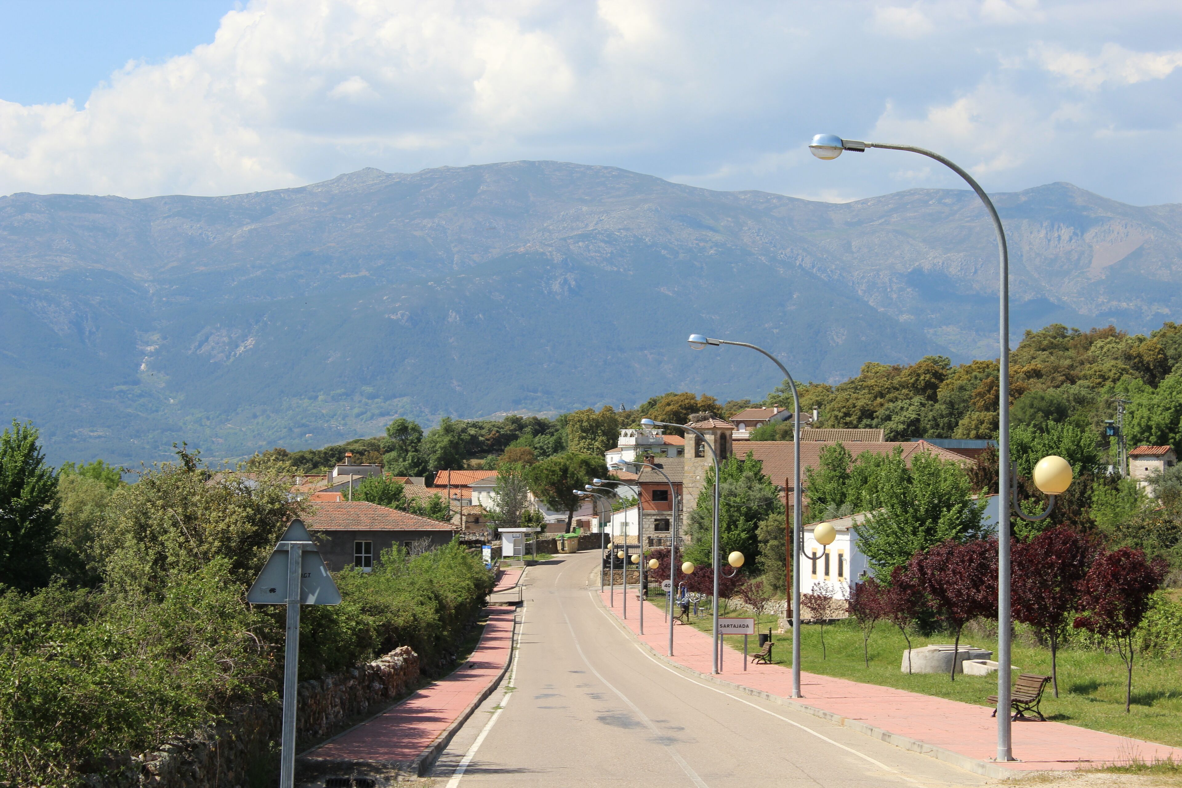 A street with houses, a bench, and mountains in the background.