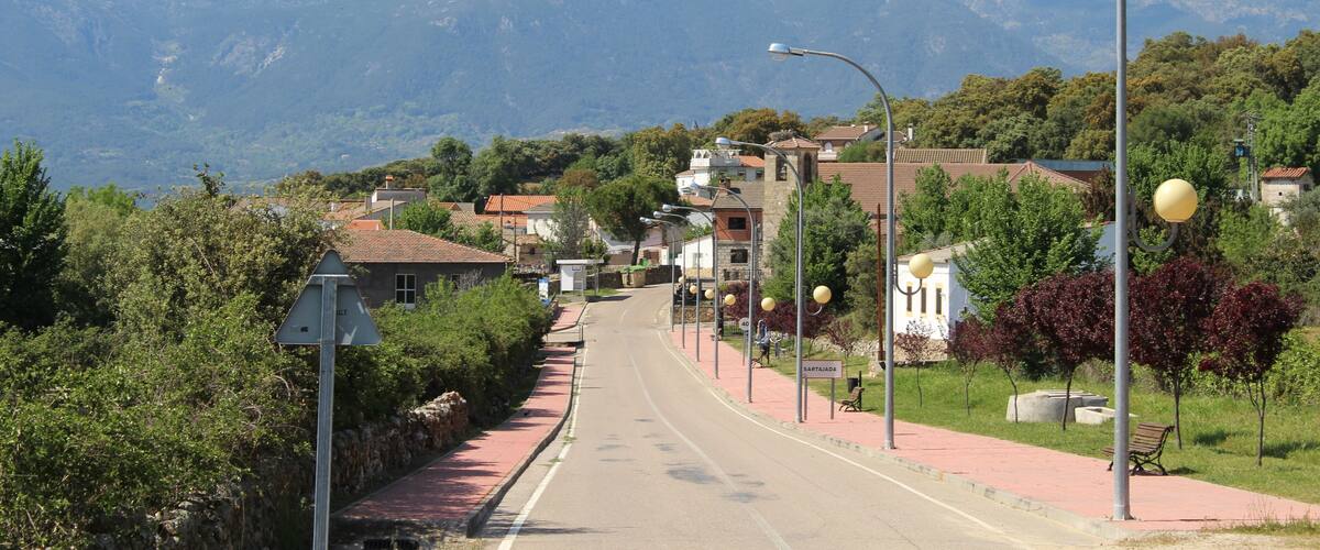 A street with houses, a bench, and mountains in the background.