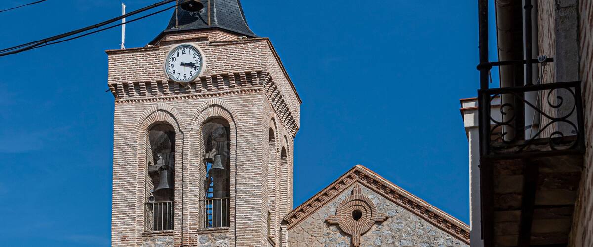 A historic stone tower with a clock, a bell, and a weather vane.