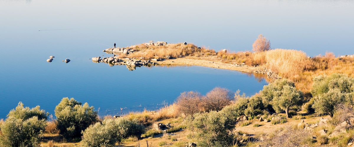 A calm lake surrounded by hills and sparse vegetation.