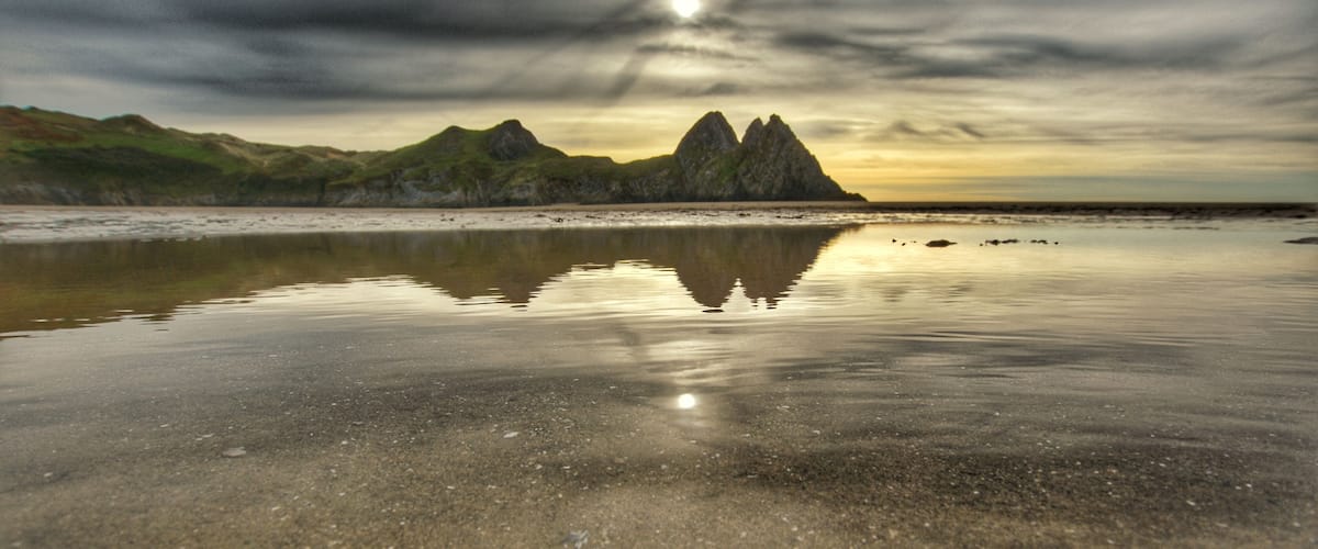 A beach with calm waters reflecting the sky and distant mountains.
