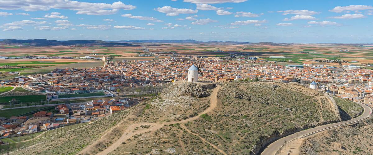 An aerial view of a town with a prominent tower, surrounded by fields and a winding road.