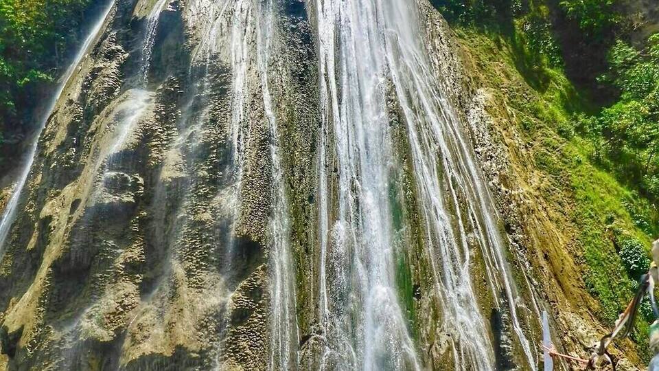 A large waterfall cascading down a rocky cliff surrounded by lush greenery.