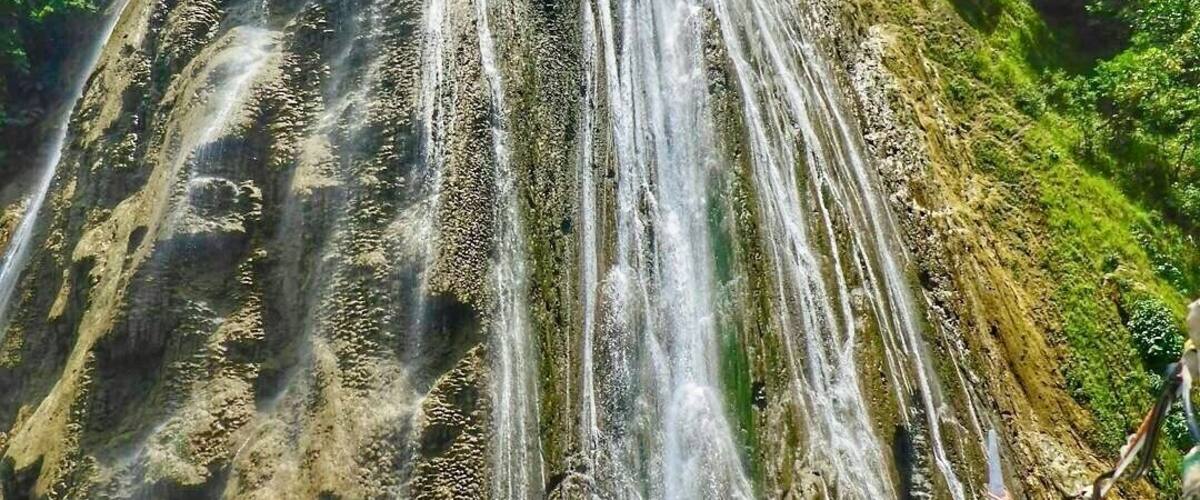 A large waterfall cascading down a rocky cliff surrounded by lush greenery.