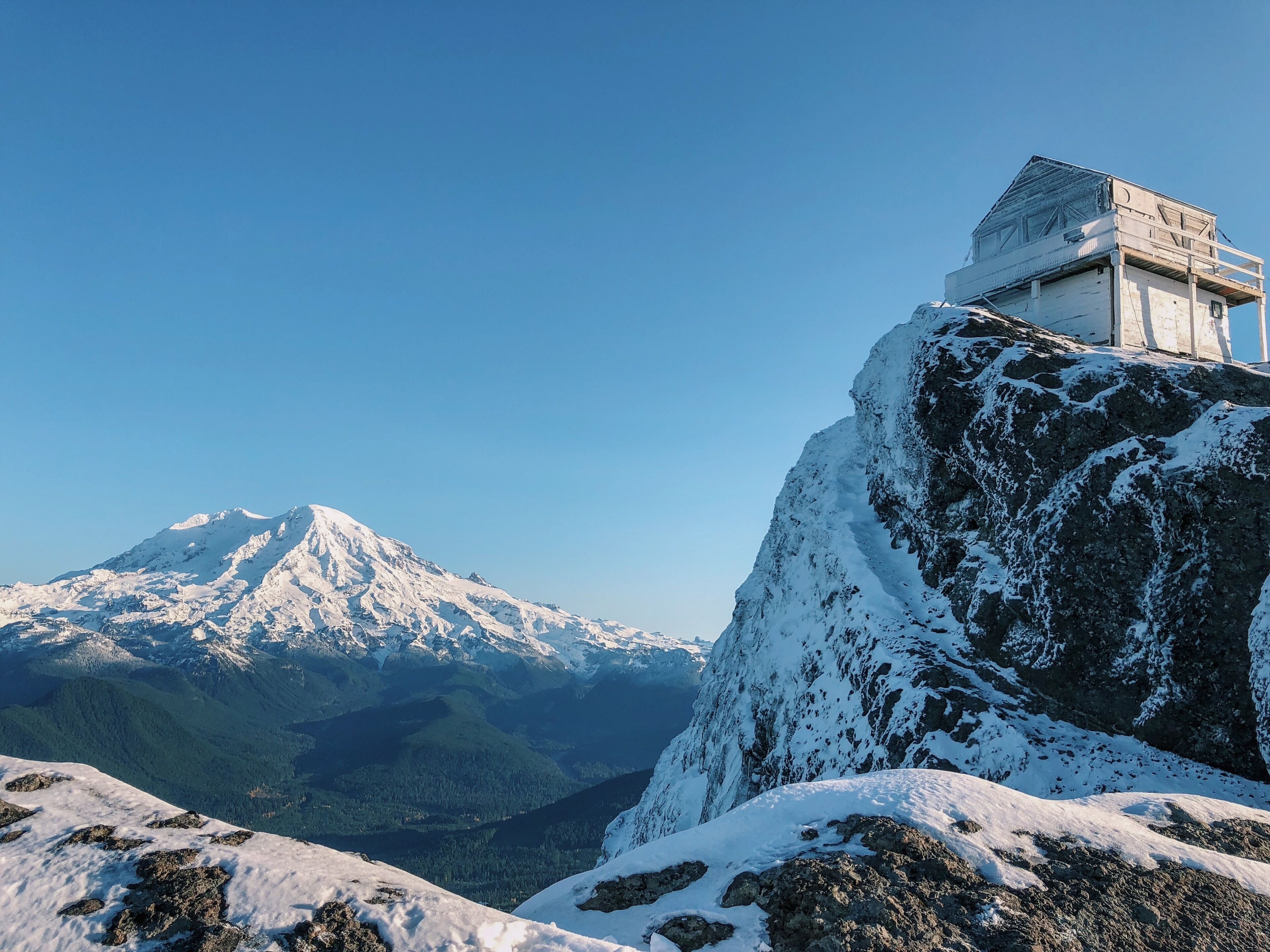 A snow-covered mountain with a cabin on a rocky outcrop.