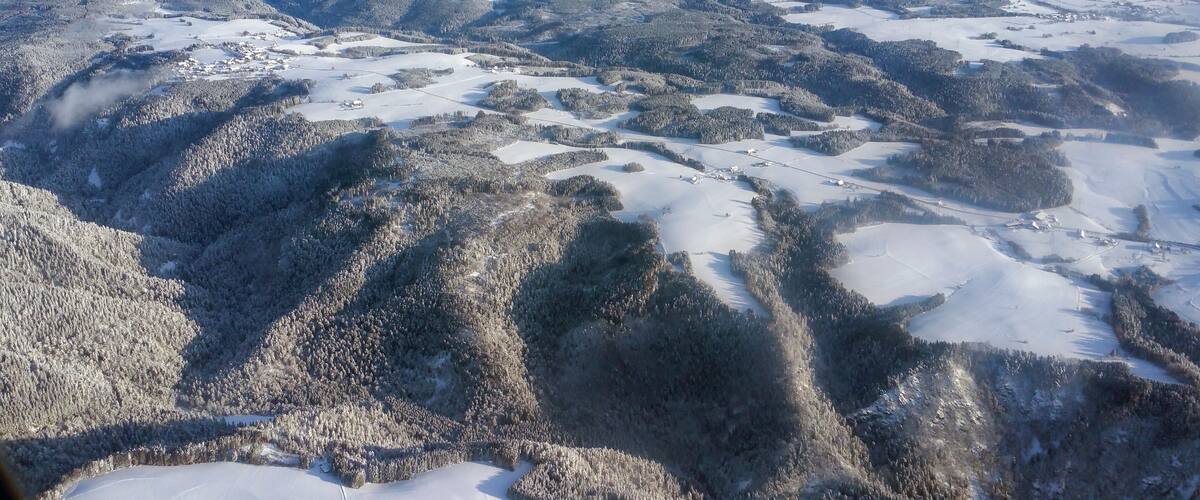A snow-covered mountainous landscape with dense forests and scattered buildings.