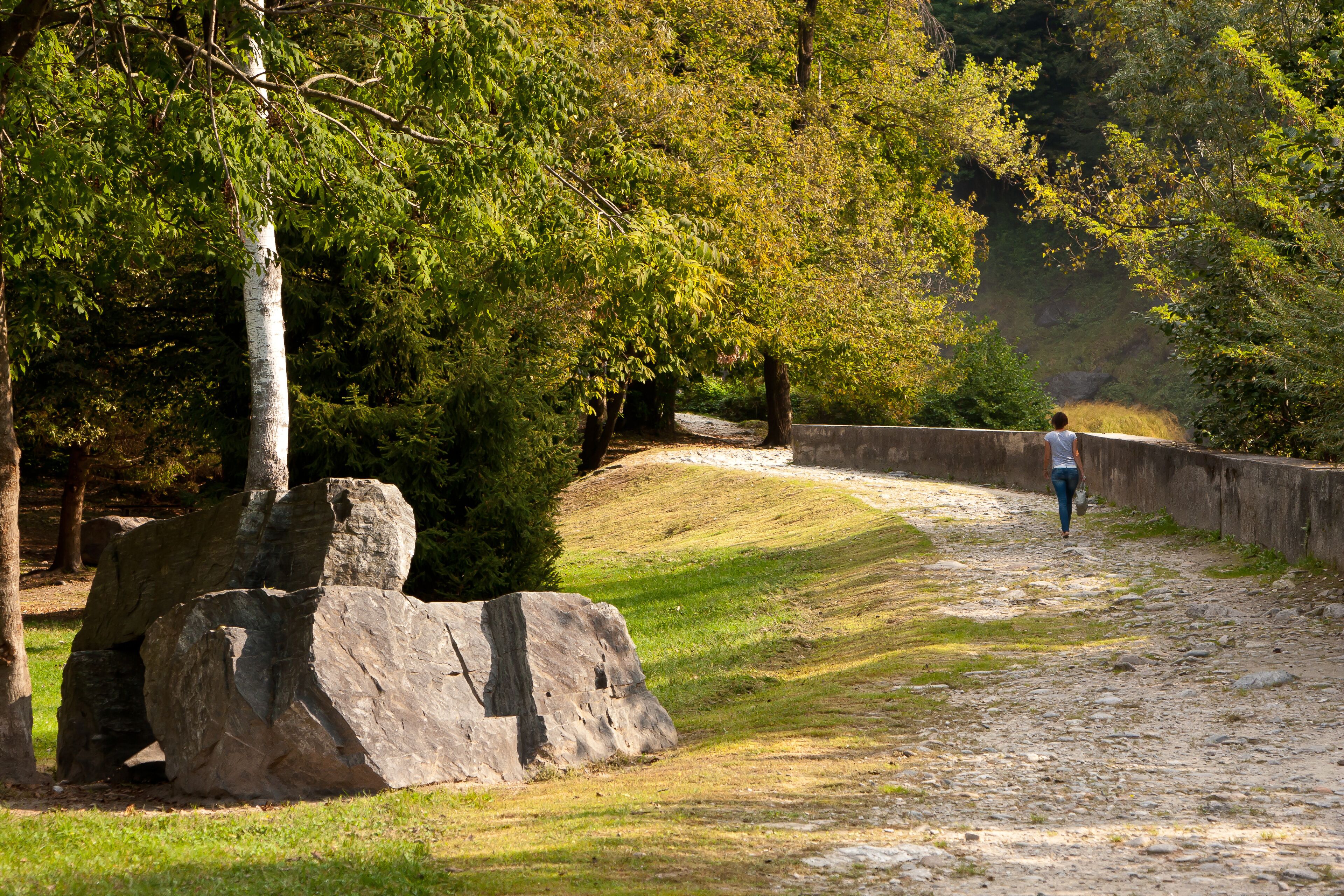 A girl walks along a path on a sunny autumn day in the valley of AcquaFraggia waterfalls in Borgonuovo - Valchiavenna, Italy