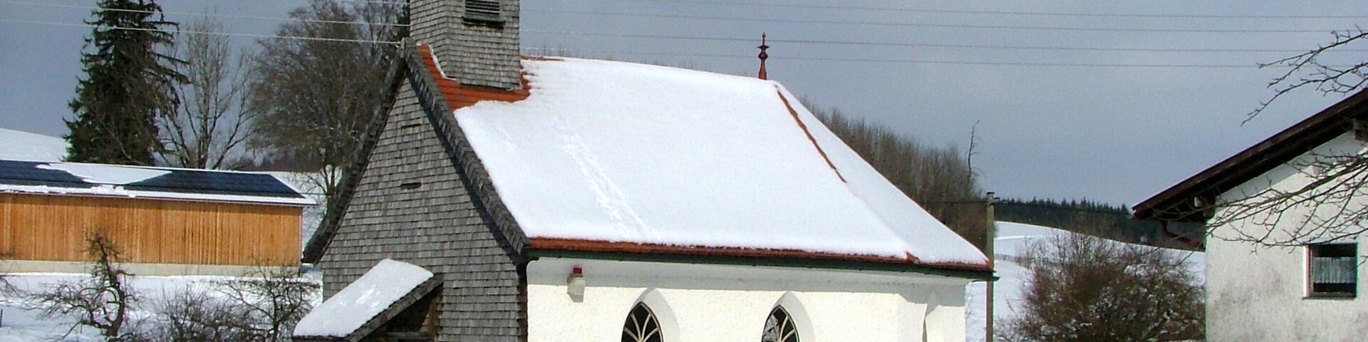 Igreja coberta de neve com um campanário e uma cerca de madeira em primeiro plano.