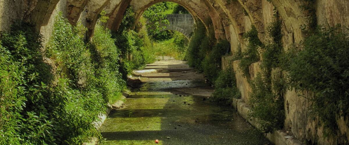 An ancient stone bridge with multiple arches, surrounded by lush greenery and a narrow waterway.