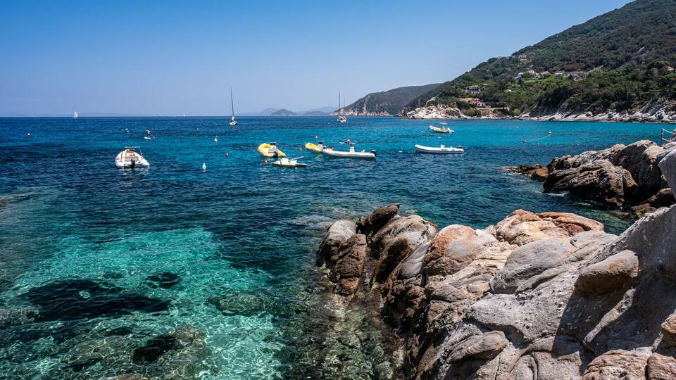 A coastal scene with clear turquoise waters, rocky shorelines, and several small boats.
